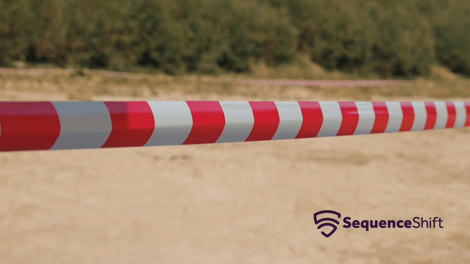 Close-up of red and white striped barrier tape stretched across a sandy field, with a second line of tape and green shrubs blurred in the background. The SequenceShift logo sits in the lower right corner.