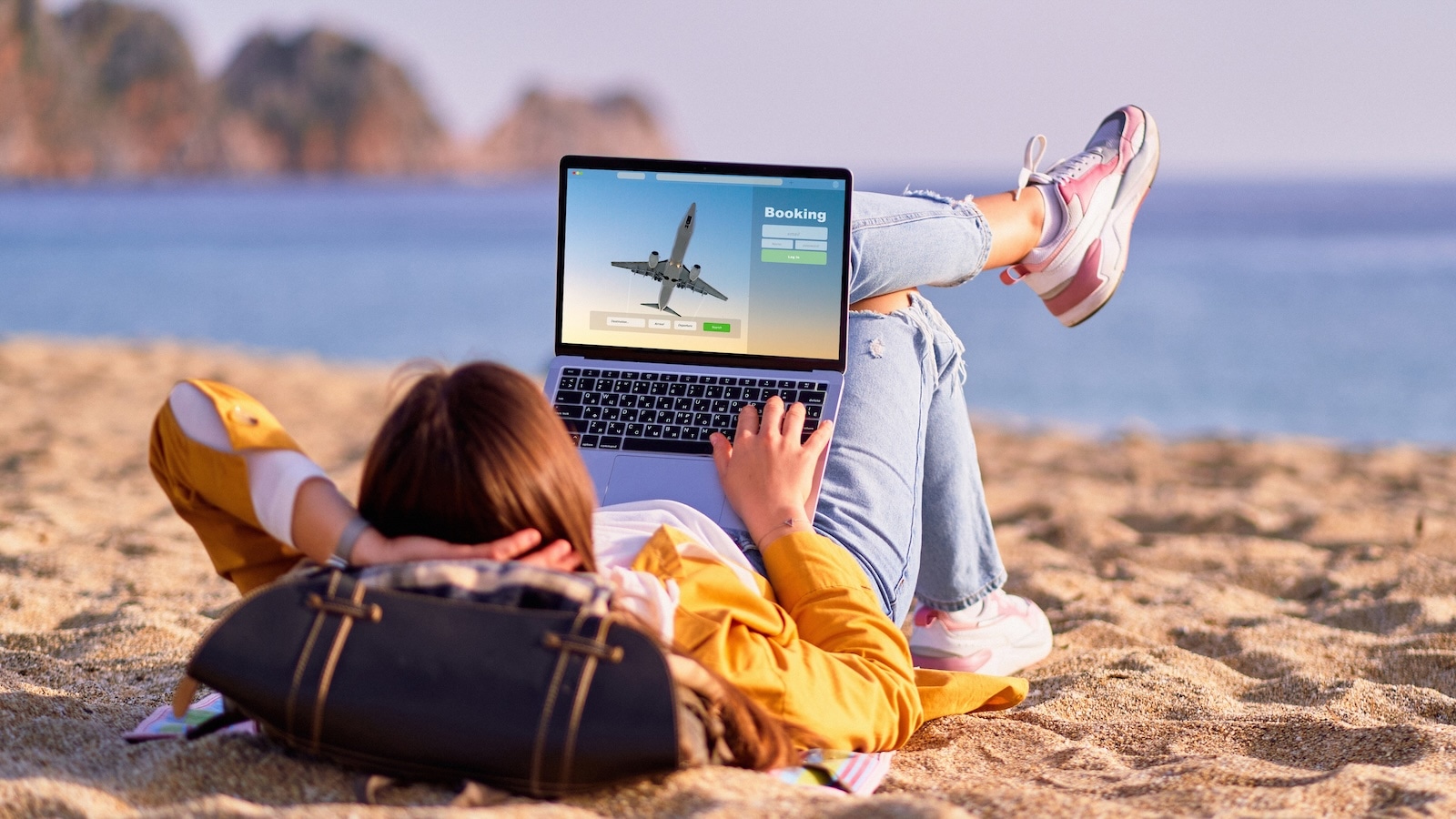 Woman on beach using laptop to complete customer journey booking