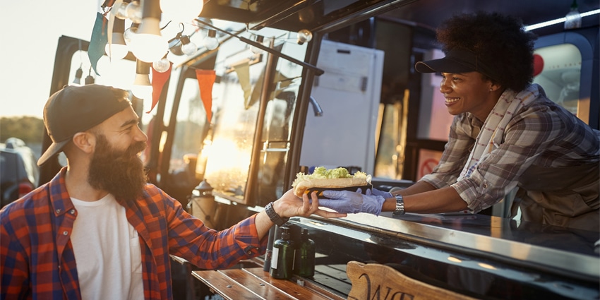 afro-american female employee gives with care sandwich to young hipster male customer