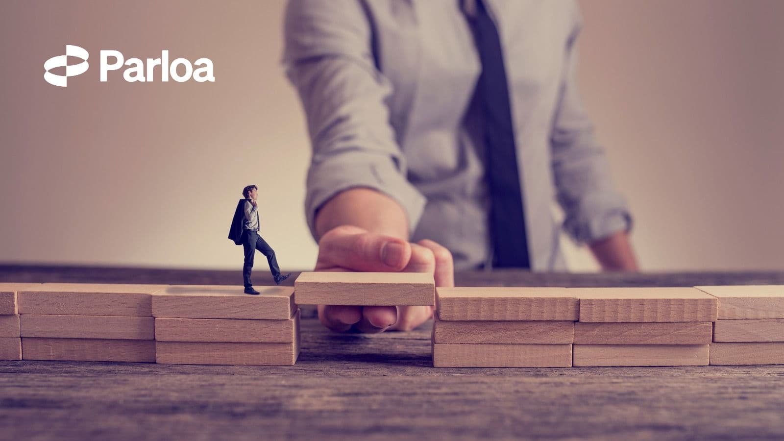 A hand places a wooden block to bridge a gap for a small figure walking across, illustrating active support helping something progress rather than being left to run on its own