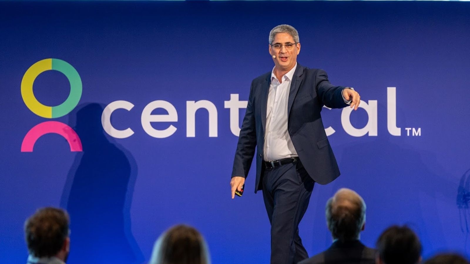 Gal Rimon, Founder & CEO of Centrical, walks across the stage gesturing towards the audience at Centrical’s Big Game event in London, in front of a large blue backdrop showing the Centrical logo